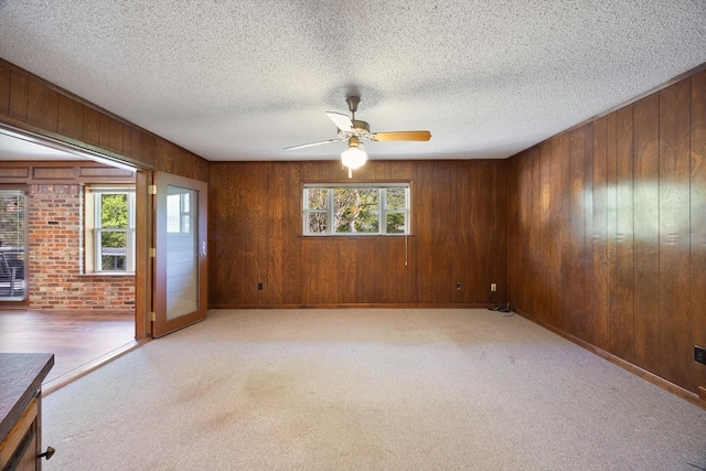 spare room featuring wood walls, ceiling fan, light carpet, and a textured ceiling