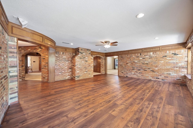 unfurnished living room with ceiling fan, wood finished floors, arched walkways, and brick wall