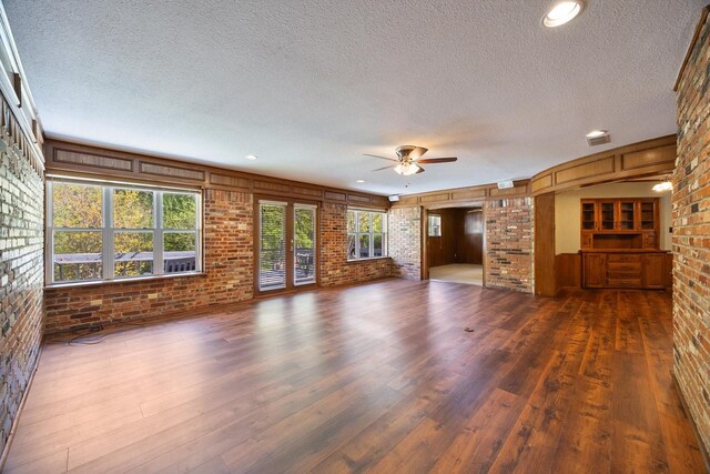 unfurnished living room with a textured ceiling, a ceiling fan, brick wall, and dark wood finished floors