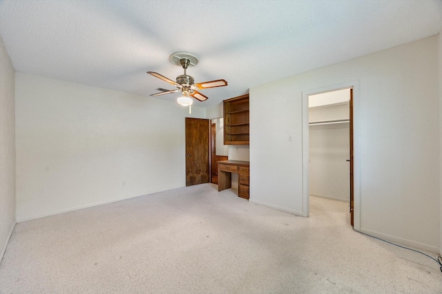 unfurnished bedroom featuring a closet, a walk in closet, a textured ceiling, and ceiling fan