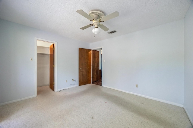 unfurnished bedroom featuring a walk in closet, a textured ceiling, carpet flooring, and visible vents