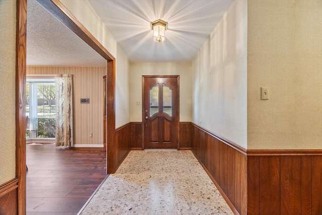 entrance foyer with wooden walls, wainscoting, wood finished floors, and a textured ceiling