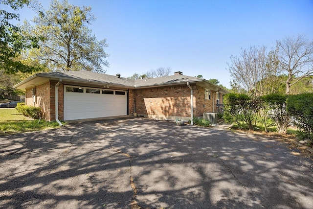view of side of home with a chimney, cooling unit, an attached garage, aphalt driveway, and brick siding
