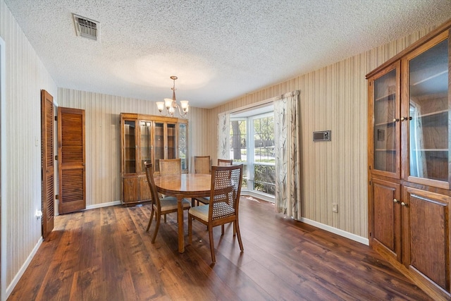 dining space featuring visible vents, baseboards, a notable chandelier, dark wood finished floors, and wallpapered walls