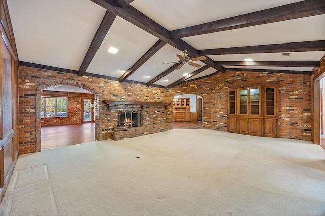 unfurnished living room with brick wall, arched walkways, ceiling fan, and carpet floors