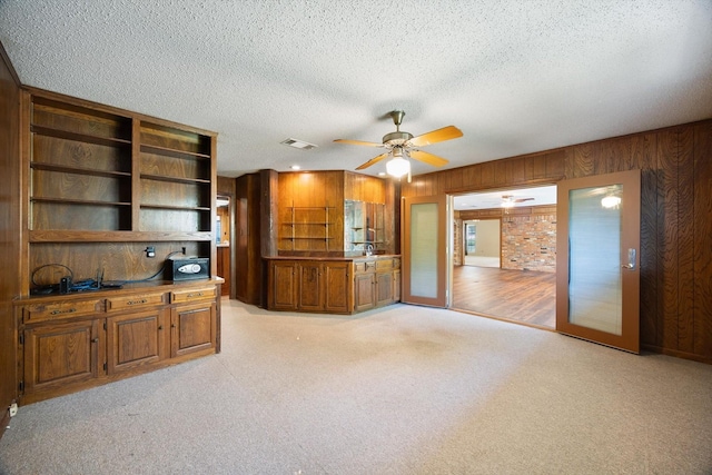 interior space with ceiling fan, a textured ceiling, visible vents, light carpet, and wooden walls