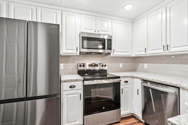 kitchen featuring appliances with stainless steel finishes, white cabinetry, decorative backsplash, light stone counters, and light wood-style flooring