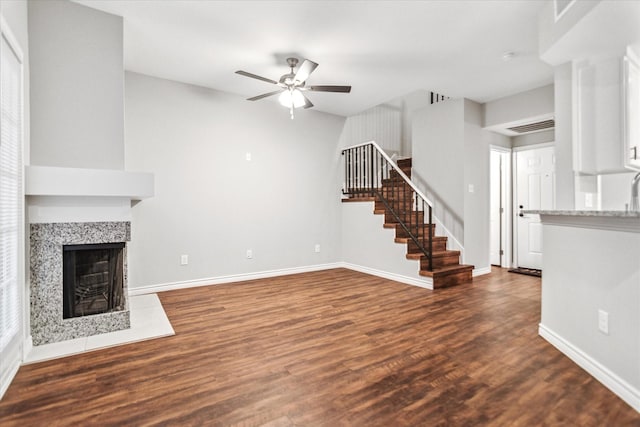 unfurnished living room featuring a ceiling fan, stairway, dark wood-type flooring, and baseboards