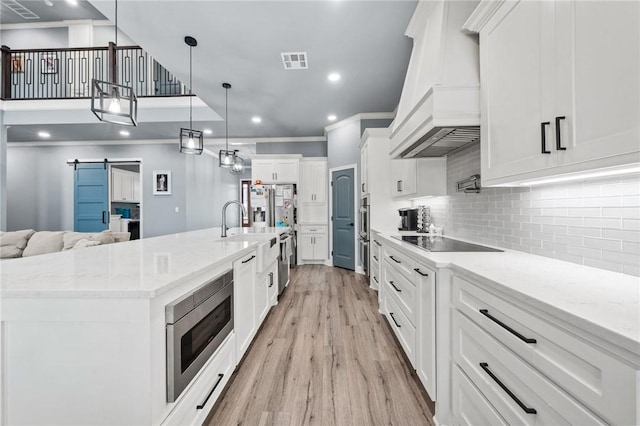 10281 Creekside Ln, Waco, TX 76712 - kitchen with custom range hood, stainless steel appliances, a barn door, light wood-type flooring, and white cabinetry
