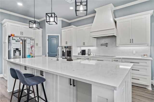 10281 Creekside Ln, Waco, TX 76712 - kitchen with custom range hood, appliances with stainless steel finishes, white cabinets, wood finished floors, and crown molding