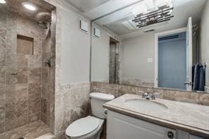 bathroom with toilet, vanity, a tile shower, and tile walls