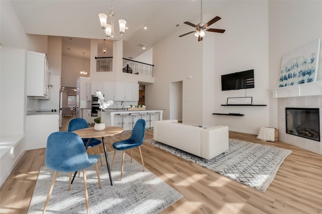 1108 Silverthorn Trl, Justin, TX 76247 - dining area featuring high vaulted ceiling, light wood-style flooring, a ceiling fan, a chandelier, and a tiled fireplace