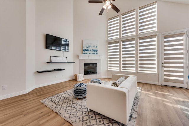 1108 Silverthorn Trl, Justin, TX 76247 - living room featuring wood finished floors, ceiling fan, a towering ceiling, baseboards, and a tile fireplace