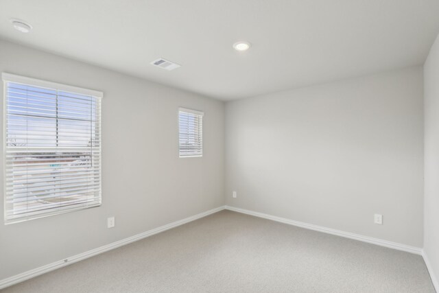 empty room with baseboards, light carpet, and visible vents