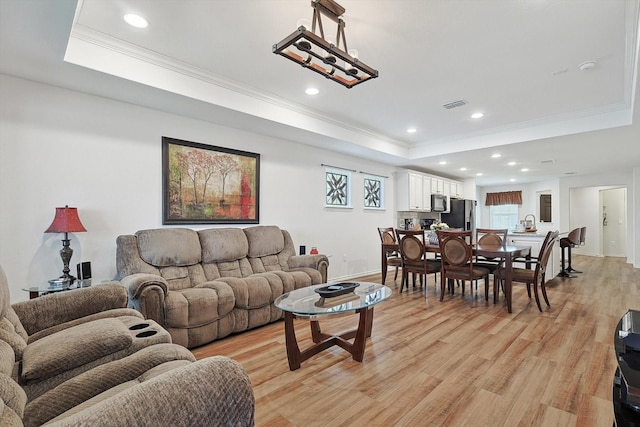 living room with recessed lighting, light wood-type flooring, a tray ceiling, and ornamental molding