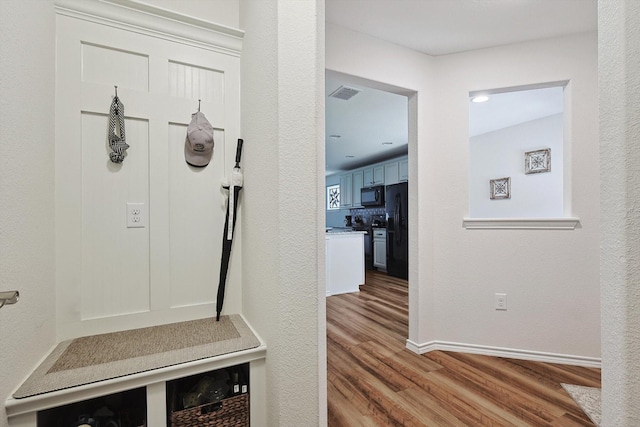 mudroom with wood finished floors, a textured wall, baseboards, and visible vents