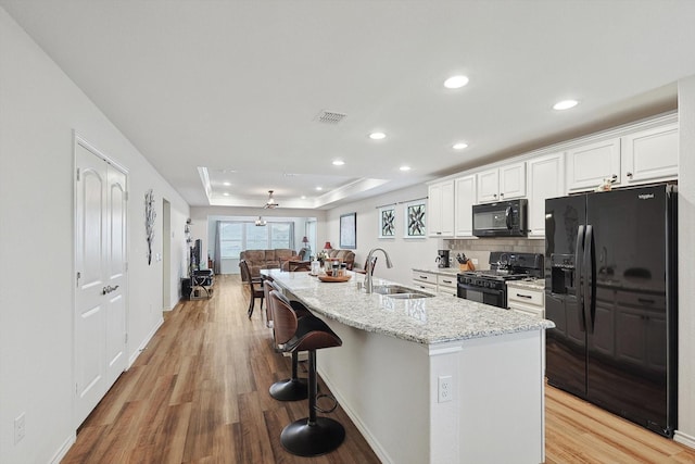 kitchen featuring visible vents, a sink, a tray ceiling, black appliances, and light wood finished floors