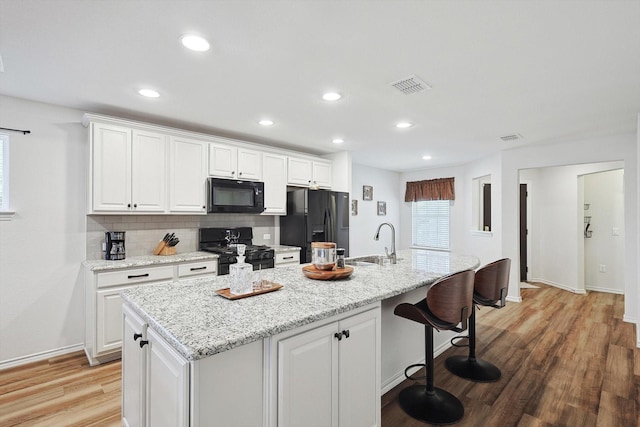 kitchen featuring visible vents, white cabinets, black appliances, and a center island with sink