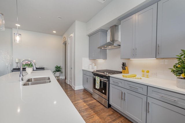 kitchen featuring a sink, dark wood-type flooring, wall chimney range hood, gray cabinetry, and gas range