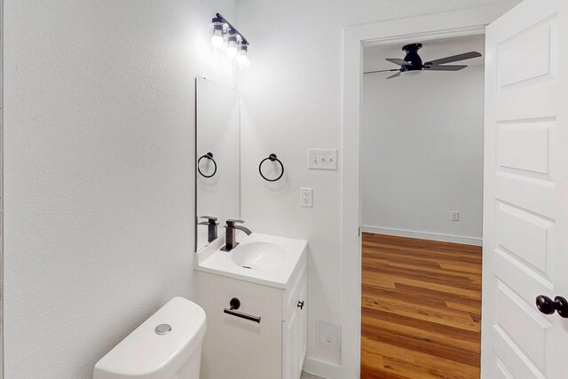 6840 Hillmont Dr, Dallas, TX 75217 - half bathroom featuring baseboards, toilet, a ceiling fan, vanity, and wood finished floors