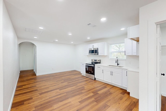6840 Hillmont Dr, Dallas, TX 75217 - kitchen featuring light wood-type flooring, white cabinets, stainless steel appliances, arched walkways, and a sink