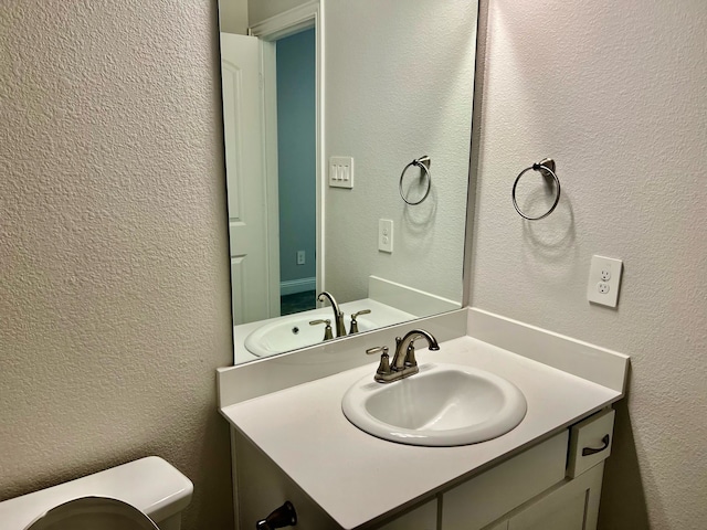 bathroom featuring a textured wall, vanity, and toilet