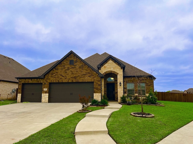 french country home featuring driveway, stone siding, a front yard, a garage, and a shingled roof