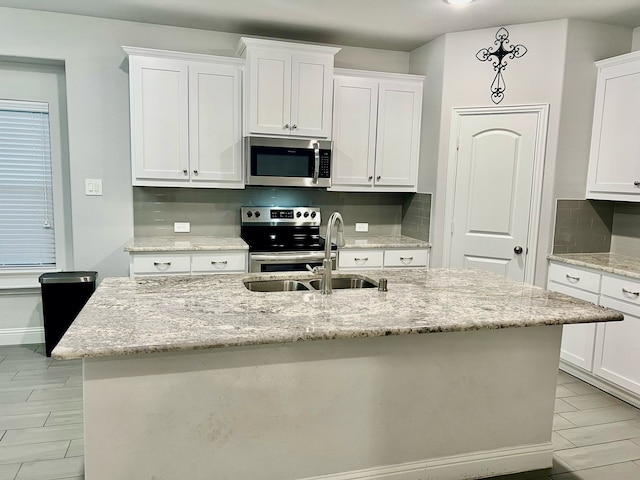 kitchen with tasteful backsplash, appliances with stainless steel finishes, a sink, and white cabinets