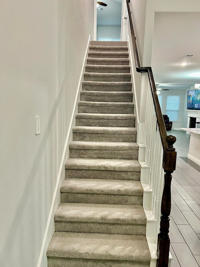 staircase featuring baseboards, a ceiling fan, wood finished floors, and a fireplace
