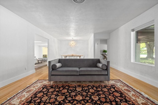 living area featuring a textured ceiling, light wood finished floors, a notable chandelier, and baseboards