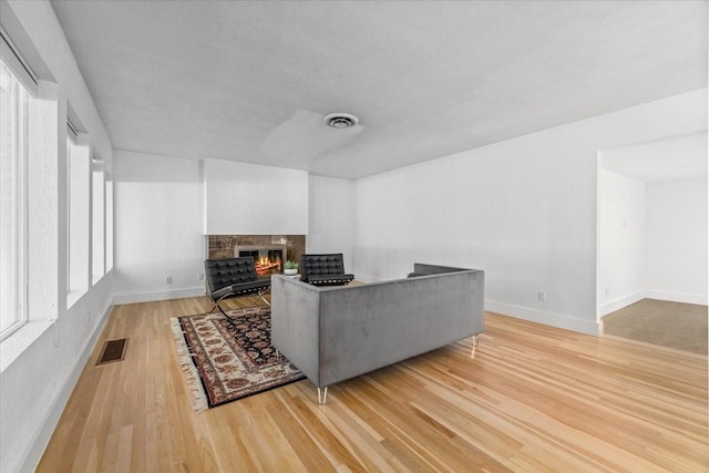 living area featuring light wood-type flooring, baseboards, a glass covered fireplace, and visible vents