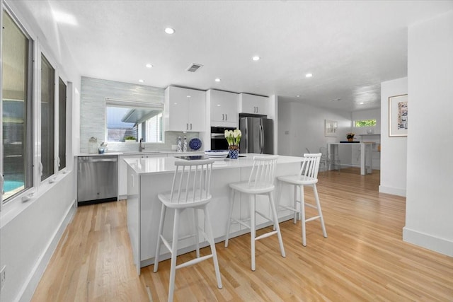 kitchen featuring a kitchen bar, white cabinetry, visible vents, a kitchen island, and appliances with stainless steel finishes
