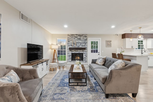 living room featuring visible vents, recessed lighting, light wood-style flooring, and a stone fireplace