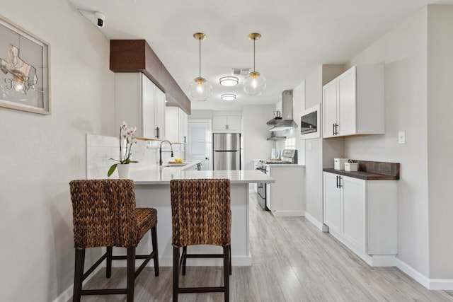 kitchen with gas range, light wood-style floors, wall chimney range hood, a sink, and a peninsula