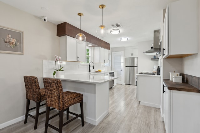 kitchen with appliances with stainless steel finishes, backsplash, a sink, visible vents, and a peninsula