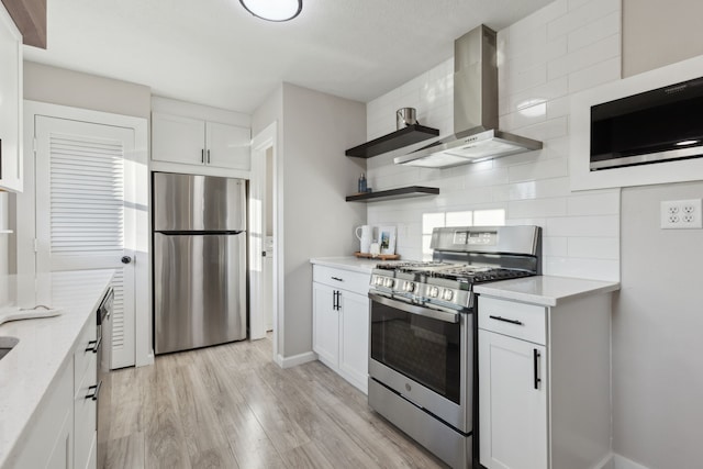 kitchen featuring tasteful backsplash, open shelves, appliances with stainless steel finishes, wall chimney range hood, and light wood finished floors