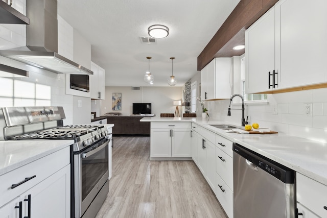 kitchen with wall chimney range hood, tasteful backsplash, a sink, appliances with stainless steel finishes, and open floor plan