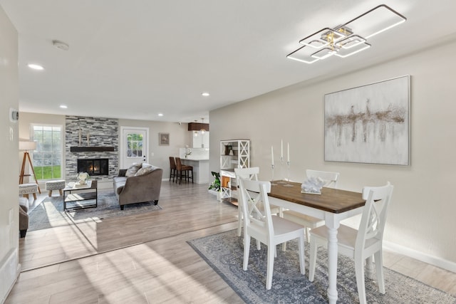 dining room with recessed lighting, a fireplace, a notable chandelier, baseboards, and wood finished floors