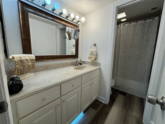 13633 Weald Green St, Dallas, TX 75240 - bathroom with toilet, vanity, wood finished floors, a shower with shower curtain, and a textured wall