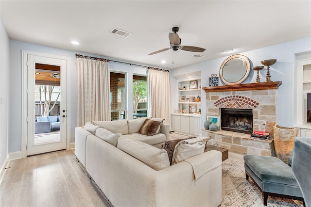 living room featuring light wood finished floors, a ceiling fan, visible vents, and a stone fireplace