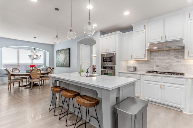 kitchen featuring a sink, arched walkways, appliances with stainless steel finishes, light countertops, and under cabinet range hood