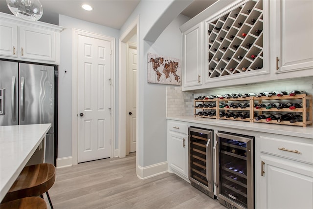 bar with recessed lighting, freestanding refrigerator, beverage cooler, and light wood finished floors