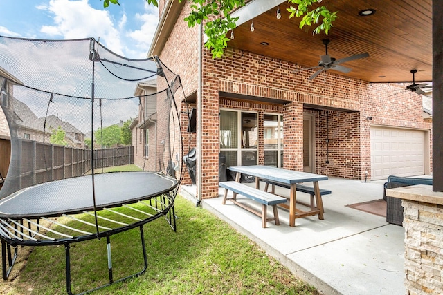 view of patio / terrace featuring a garage, a trampoline, fence, and a ceiling fan