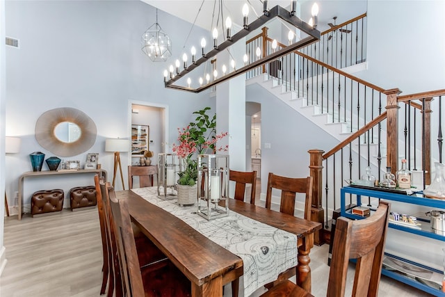 dining room featuring stairway, a high ceiling, wood finished floors, visible vents, and a notable chandelier
