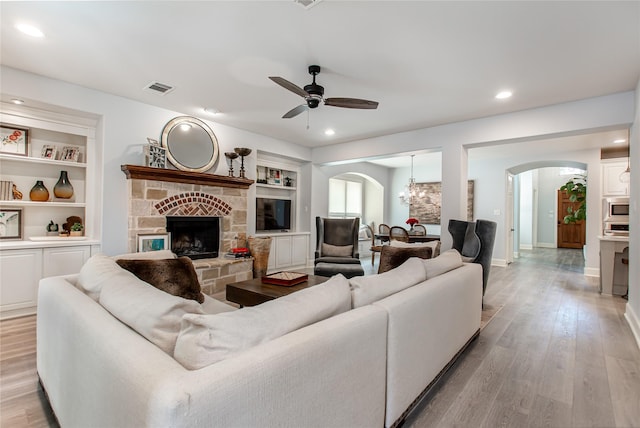 living room with arched walkways, visible vents, built in features, light wood-style floors, and ceiling fan with notable chandelier