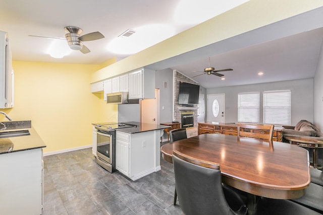 7820 Prairie Dr, Watauga, TX 76148 - kitchen with stainless steel appliances, ceiling fan, dark countertops, white cabinetry, and a large fireplace