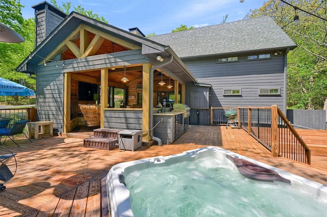 back of property featuring roof with shingles, a wooden deck, a chimney, and hot tub deck surround
