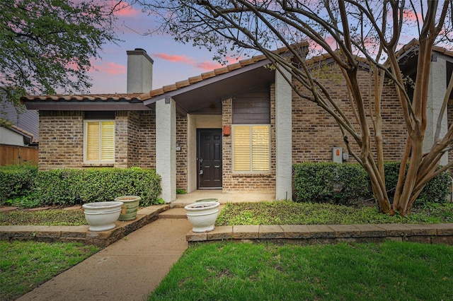 exterior entry at dusk with brick siding and a chimney