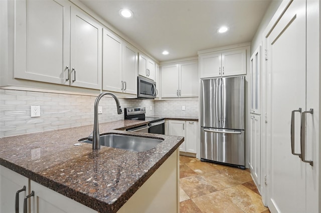 kitchen featuring tasteful backsplash, white cabinets, a sink, appliances with stainless steel finishes, and dark stone counters