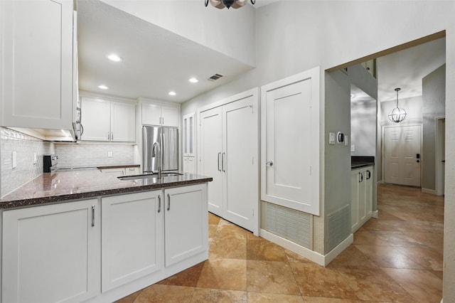 kitchen with a peninsula, backsplash, white cabinets, appliances with stainless steel finishes, and a sink